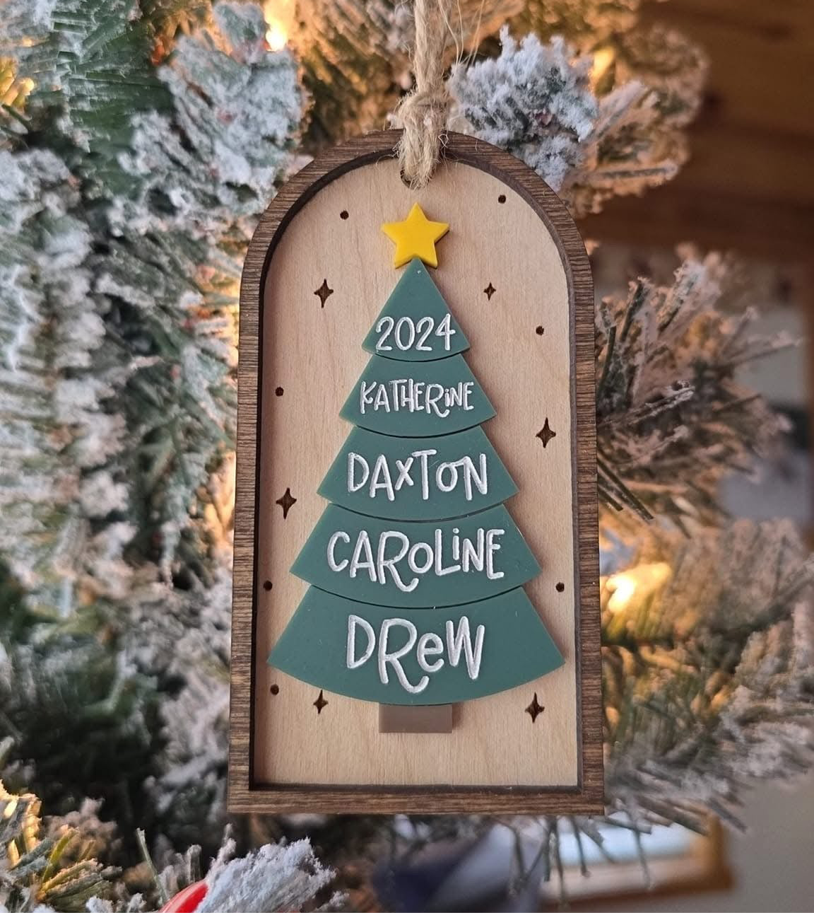 Wooden ornament with Christmas tree design and names, hanging on a decorated tree.