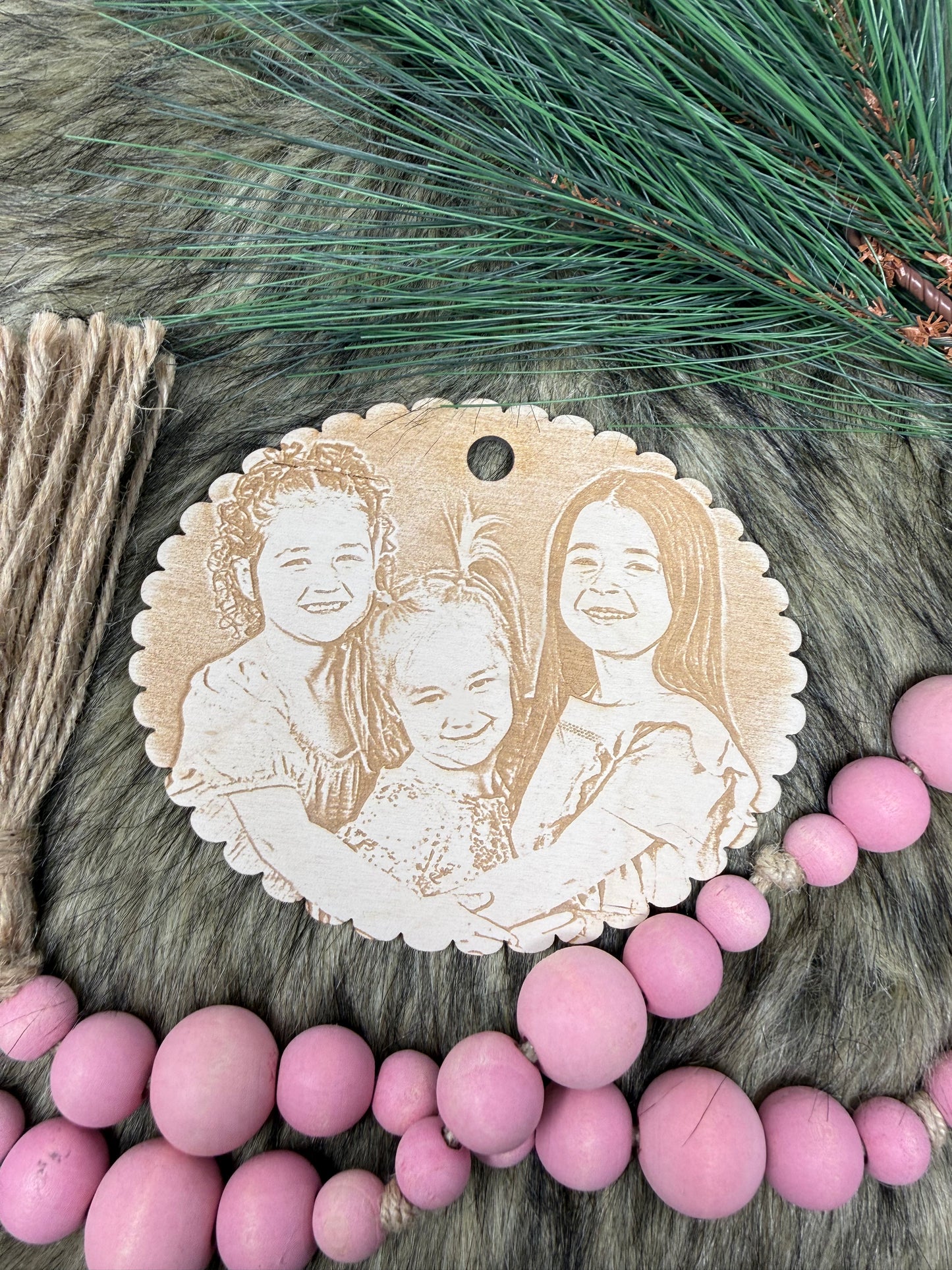 Decorative ornament with engraved faces on a textured surface with pink beads and greenery.