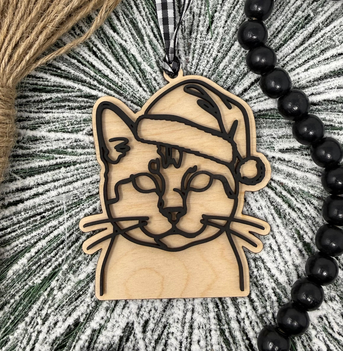 Wooden ornament with cat design on a textured surface with beads and yarn.