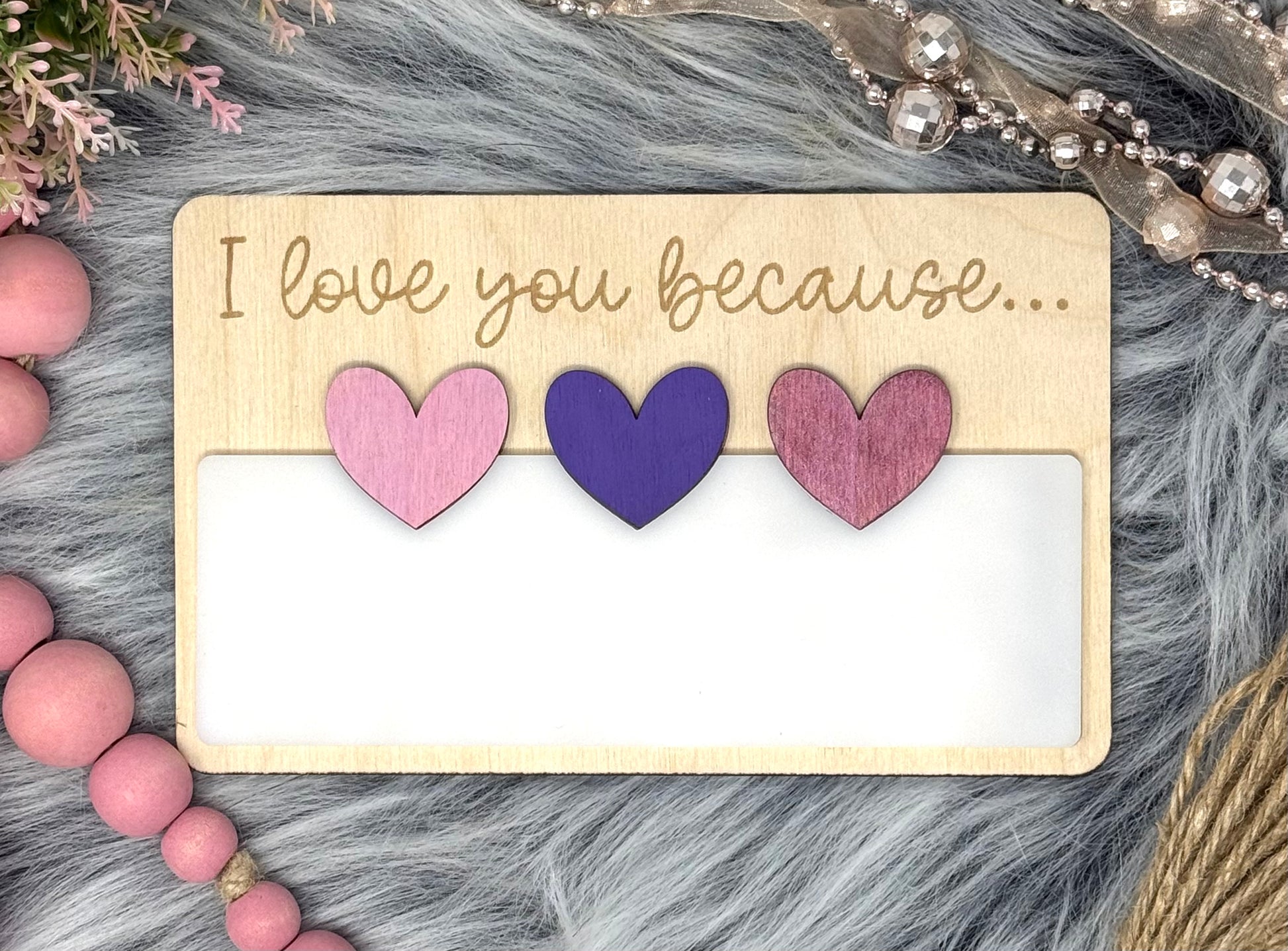 Wooden card with hearts and 'I love you because...' text on a textured surface.