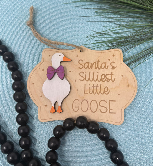 Decorative tag with a goose illustration and text 'Santa's Silliest Little Goose' on a textured blue background.