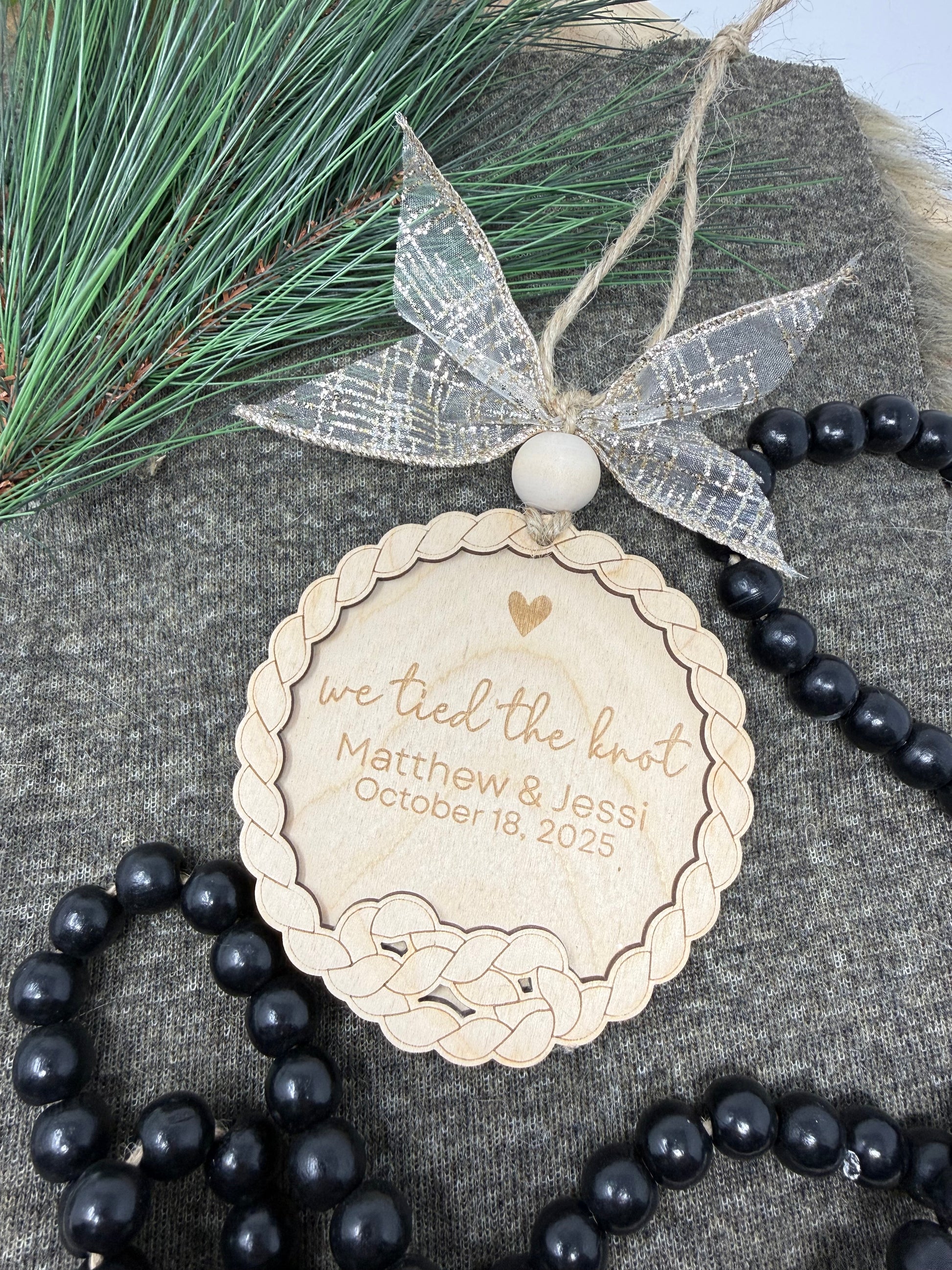 Personalized wooden round tag with engraved text, black beads, and greenery on a textured surface.